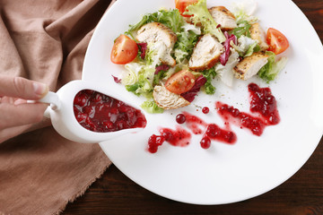 Woman pouring cranberry sauce onto plate with salad