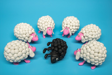 Concept - A group of white polymer clay sheep surrounding a black sheep lying on its side