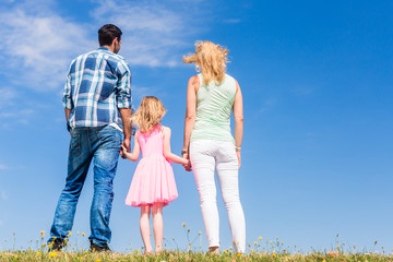 Fototapeta premium Family standing with their backs to the camera in front of blue skies