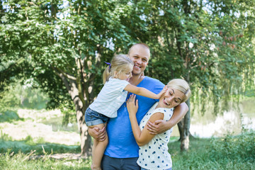 Happy mother, father and daughter in the park. Beauty nature scene with family outdoor lifestyle. Happy family together on the grass, having fun outdoor. Happiness and harmony in family life.