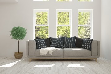 Fototapeta premium White room with sofa and green landscape in window. Scandinavian interior design. 3D illustration
