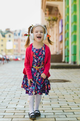 Fashion little girl with headphone listening music and dancing outdoor