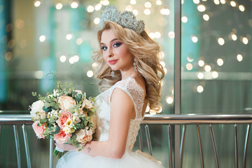 Beautiful young girl in wedding dress and crown on head with bouquet of flowers