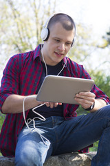 Young man with headphones sitting, listening to music and holding a tablet
