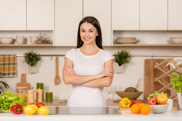 Young woman standing near desk in the kitchen, smiling, looking at camera