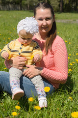 Mom and daughter sitting on green grass with yellow flowers.