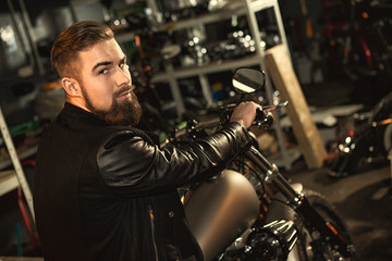 Fototapeta na wymiar Handsome bearded man on his motorbike at the workshop