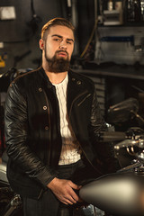 Handsome bearded man on his motorbike at the workshop