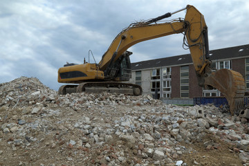 Excavator is on a pile of bricks of a destroyed house