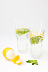Homemade lemonade with water, lemon and mint leaves in two glasses on a white background.