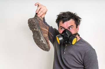 Man with gas mask is holding dirty stinky shoe - obrazy, fototapety, plakaty