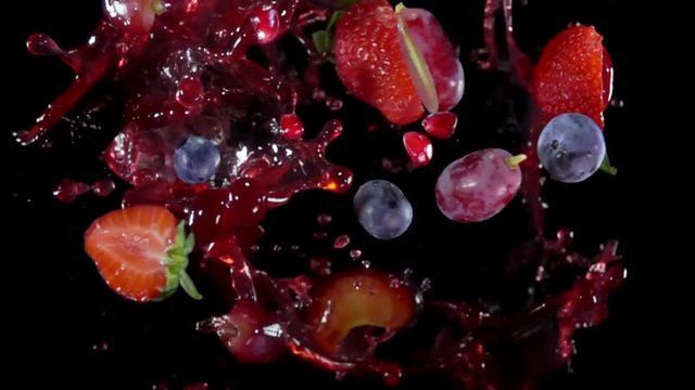 Mixed berries with juise flies to the camera on a black background in slow motion