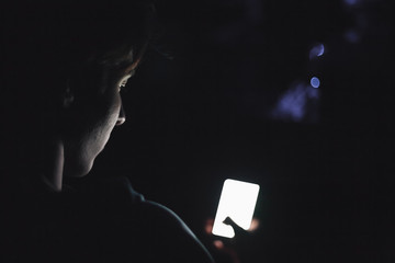 Teenage boy using smart phone in the dark