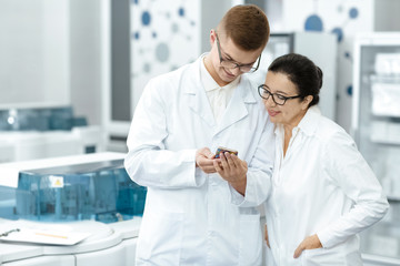 Young male scientist showing something on his smart phone to his senior colleague