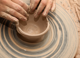 Woman in process of making clay bowl on pottery wheel