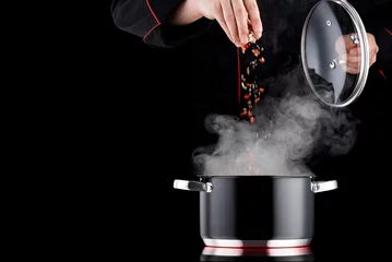 Fotobehang Koken Moderne chef-kok in professioneel uniform die kruiden toevoegt aan de dampende pot