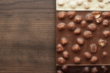 black, milk and white chocolate bars with whole hazelnuts on wooden table