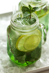 Tasty cold fresh drink lemonade with lemon, mint, ice and lime in glass on white table. Closeup.