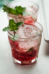 Tasty cold fresh drink lemonade with raspberry, mint, ice and lime in glass on white table. Closeup.