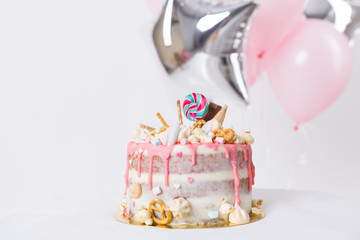 birthday cake with decorated with candies, lollipop, marshmallows. Pink pastel color. Balloons on background