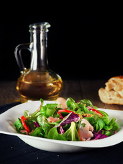 Salad of green vegetables with prosciutto on a white plate with olive oil.Rustic.Selective focus. The vertical frame.