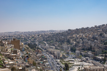 Fototapeta na wymiar View of Amman's modern and older buildings including the Roman Theater below from the hill of Amman Citadel. Hazy blue sky is above.