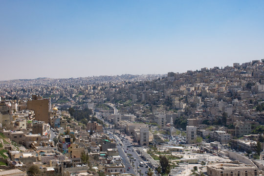 View of Amman's modern and older buildings including the Roman Theater below from the hill of Amman Citadel. Hazy blue sky is above.