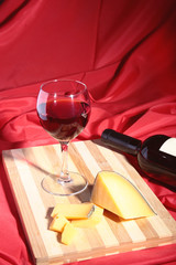 Bottle and Glass with red wine grapes and chees on wooden table.