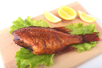 Smoked fish and lemon on green lettuce leaves on Wooden cutting board isolated on white background.