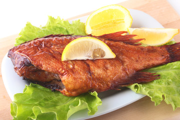 Smoked fish and lemon on green lettuce leaves on Wooden cutting board isolated on white background.