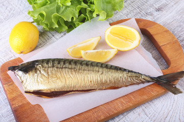 Smoked mackerele and lemon on green lettuce leaves on Wooden cutting board isolated on white background.