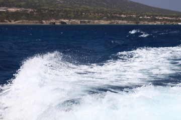 White waves from a yacht on a dark blue sea against the backdrop of the island of Cyprus