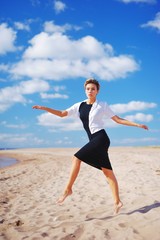 Fototapeta premium Portrait of a sad slender young woman with short hair, with outstretched hands, Bouncing on the sand, on blurred blue sky background
