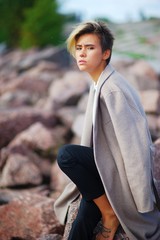 Young pretty girl with closed eyes in a draped over the shoulders of a coat sitting on a rock...