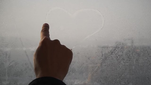 finger draws heart at a window