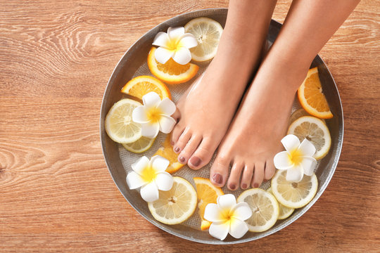 Female feet in spa bowl with citrus fruits on wooden background