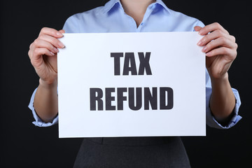 Woman holding paper sheet with text TAX REFUND on black background