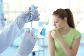 Hands of doctor preparing for vaccination and blurred patient on background