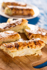 Sliced homemade cheese pie on the round wooden board with blurred background