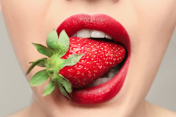 Beautiful young woman with strawberry in mouth, closeup