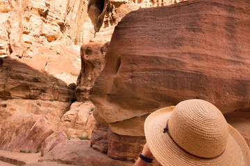 Woman wearing a straw hat looking up at the colorful sandstone in Al-Siq, Petra Jordan. The woman...
