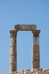 Fototapeta na wymiar Close up of columns of ancient Roman Temple of Hercules with stone beam or lintel on carved capitals at the Citadel against a deep blue cloudless sky.