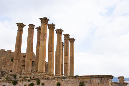 The ancient Roman Temple of Artemis with columns and carved capitals on a platform against a light blue sky with clouds. Photographed in Jerash, Jordan.