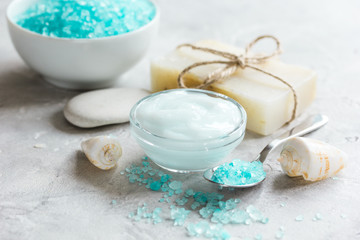 Obraz na płótnie Canvas blue bath salt, body cream and shells for spa on gray table background