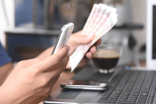 Concept,Hand holding money to paying via smartphone or laptop computer