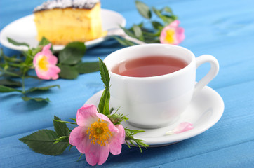 Hot tea with cheesecake and wild rose flower on boards