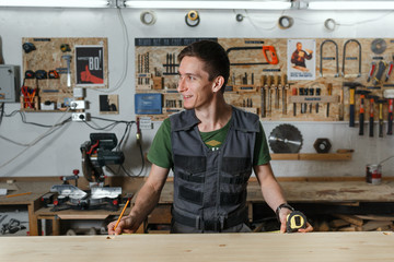 A professional carpenter in the workshop makes measurements of the product with a measuring tape measure and smiles