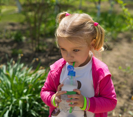 Small cute girl drinking water from plastic bottle. Green sunny photo