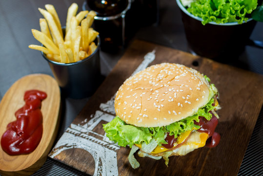 Delicious homemade hamburger with French fries, ketchup, mustard and fresh vegetables on a wooden board