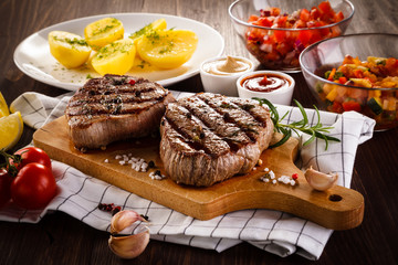 Grilled beefsteaks on cutting board on wooden table - dinner preparation